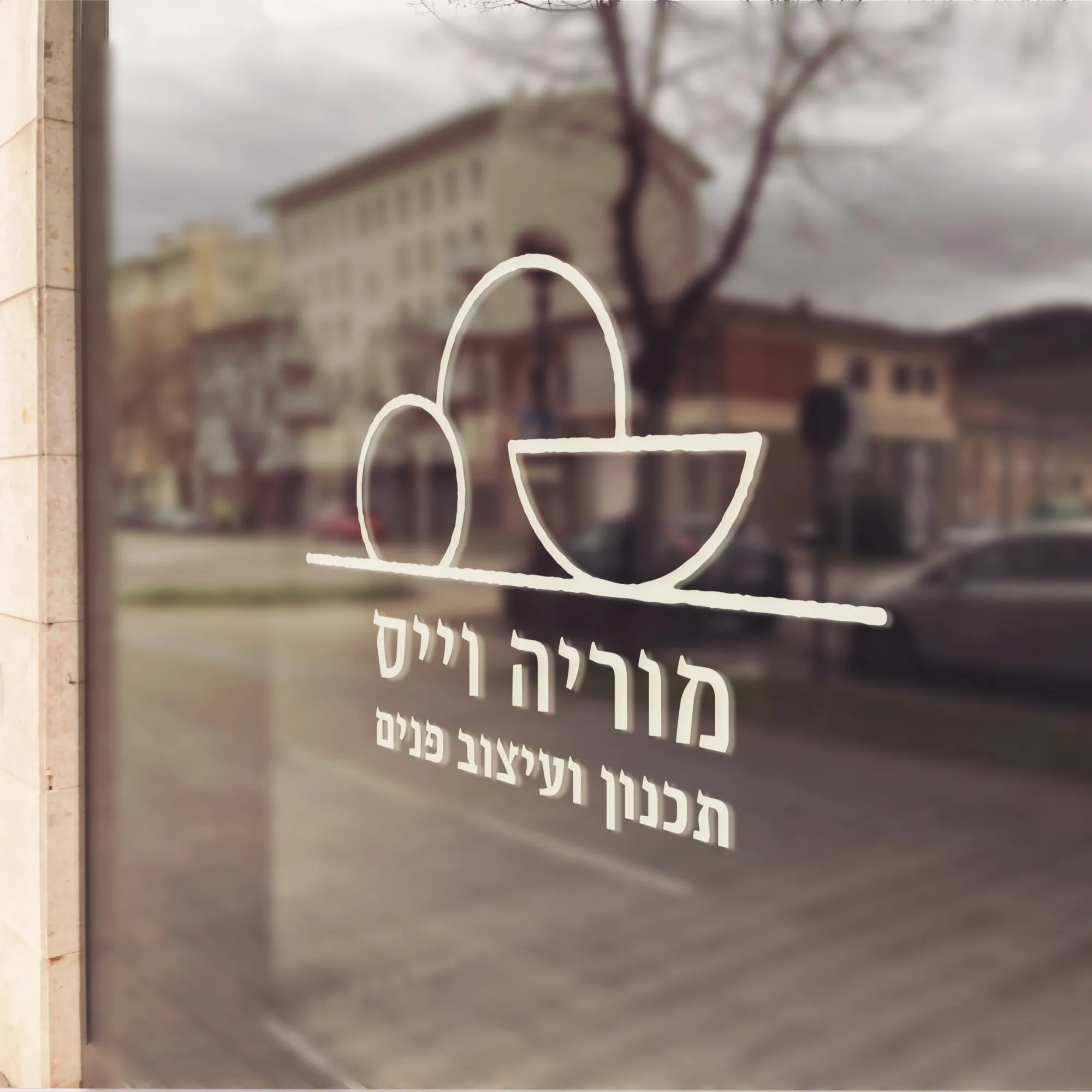 לוגו מוריה וייס כמדבקה לבנה על זכוכית חלון מול רחוב